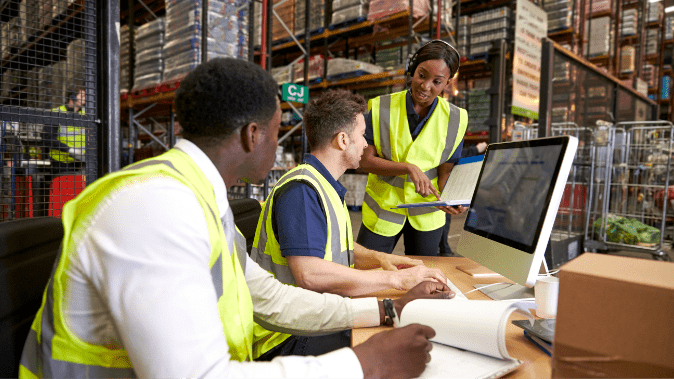 2 male warehouse employees taking instruction from female worker