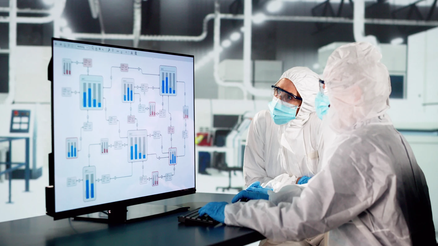 Two highly skilled workers collaborating over a computer at a sterile semiconductor factory.