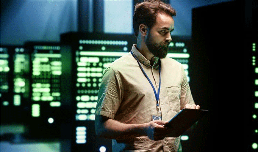 Cloud infrastructure: bearded white man with tan short-sleeve shirt stands in a data center looking at a server
