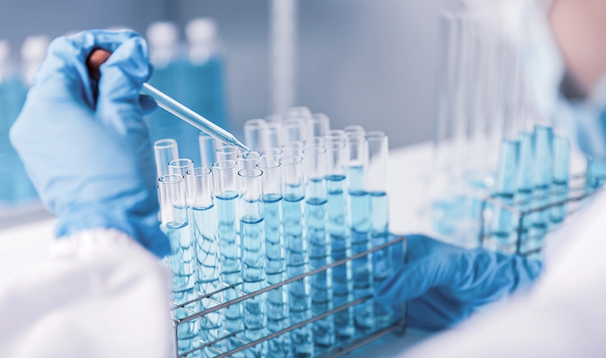 AI in drug development: a tray of test tubes with a gloved hand adding liquid to one tube with eyedropper. 