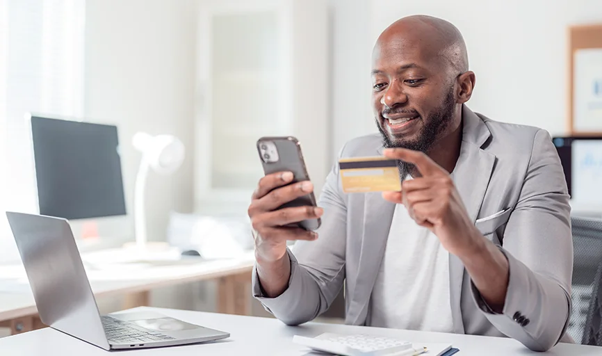 Smiling African American man with credit card and cell phone enjoying easy transaction due to platform modernization