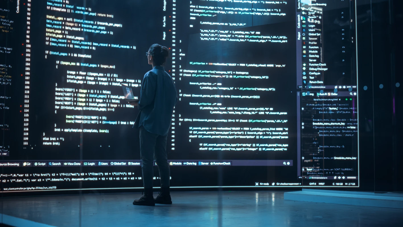 A man stands facing three wall-sized computer screens full of business intelligence.